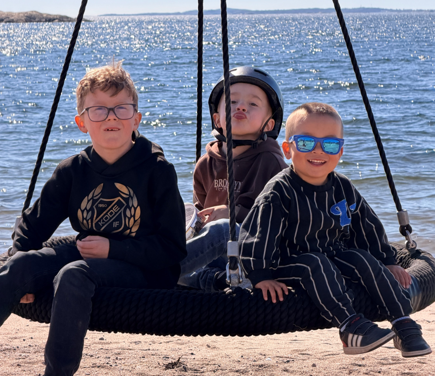 Tre killar sitter på en gunga vid havet