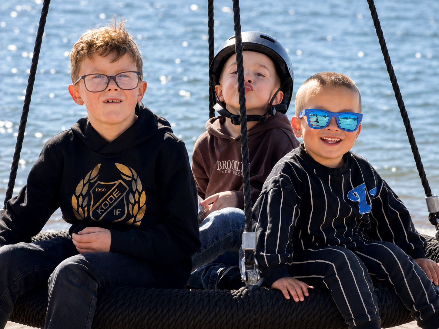 Tre killar sitter på en gunga vid havet.